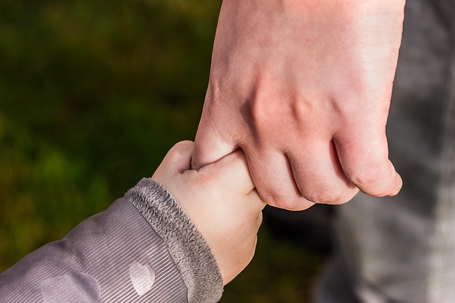 Mani di genitore e bambino intrecciate, simbolo di sostegno familiare